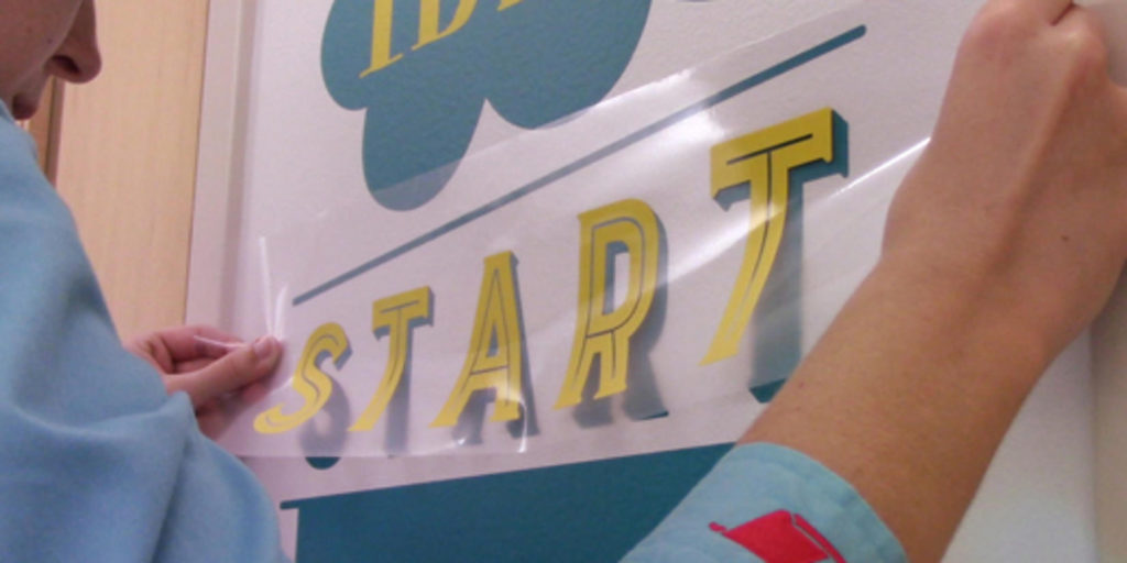 Osoba przykleja folię transferową z napisem "START" na ścianie
